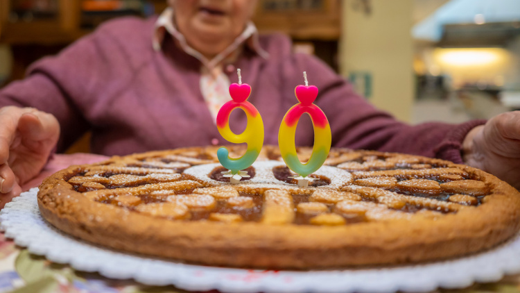 Un pastel grande con velas que indican el número 90 y una mujer frente a ella