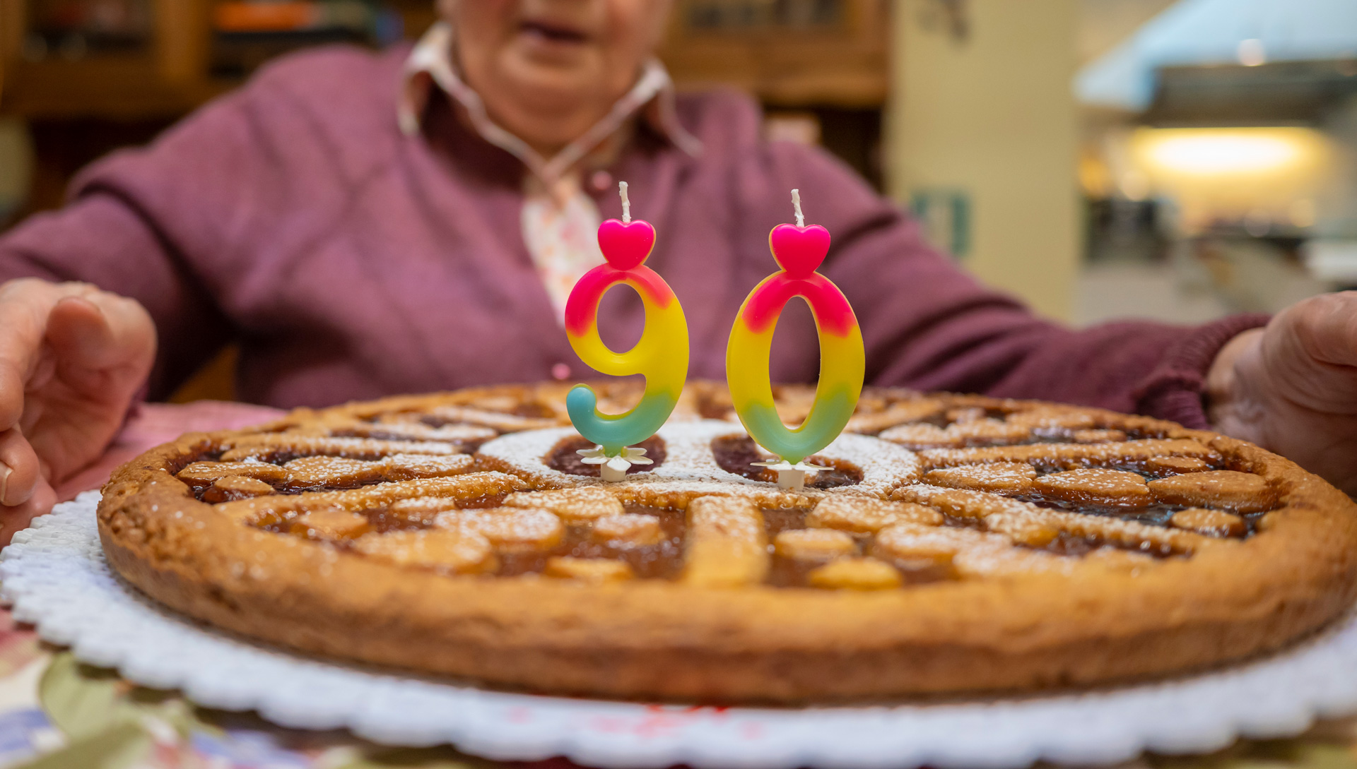 Un pastel grande con velas que indican el número 90 y una mujer frente a ella